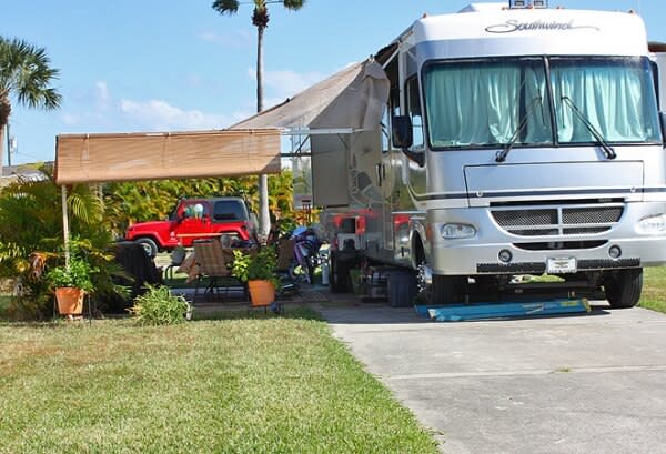 Silver motorhome with tan awning, covered patio area, red Jeep parked nearby
