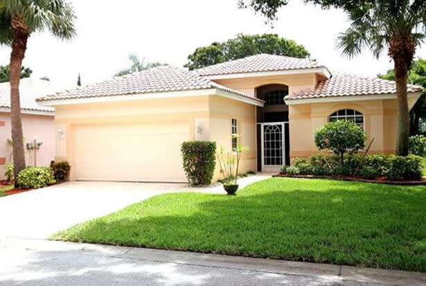 Single‑story beige home with white tile roof, palm trees, and a neat green lawn.