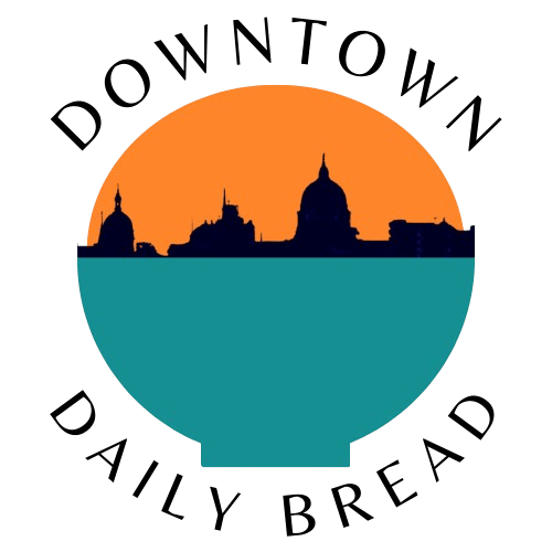 Logo that says Downtown Daily Bread in black type font, around a circled silhouette of the city, with teal and orange
