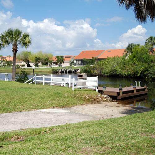 Canal boat dock with white railing, palm tree, grassy slope, and waterfront homes beyond