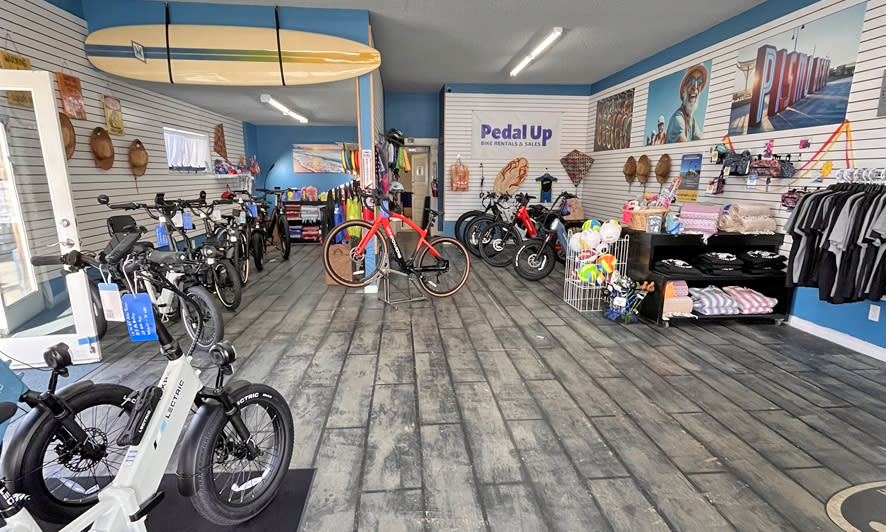 Beach-inspired Pedal Up Bike Rentals & Sales showroom featuring Lectric electric bikes and coastal merchandise on the Central