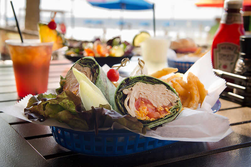 Spinach chicken wrap with onion rings and pickle in a beachside setting.