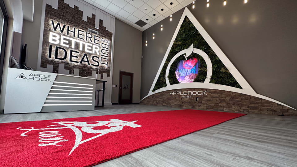 Apple Rock headquarters lobby in Greensboro, NC featuring branded signage, reception desk, red logo rug, and “Where Better Id