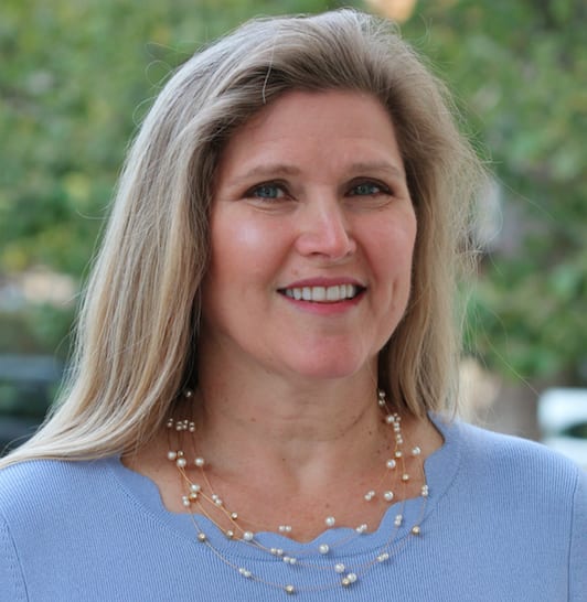 Smiling blonde woman in a blue top with pearl necklace