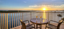 Balcony table with two champagne glasses overlooking peaceful waterway at golden hour sunset.
