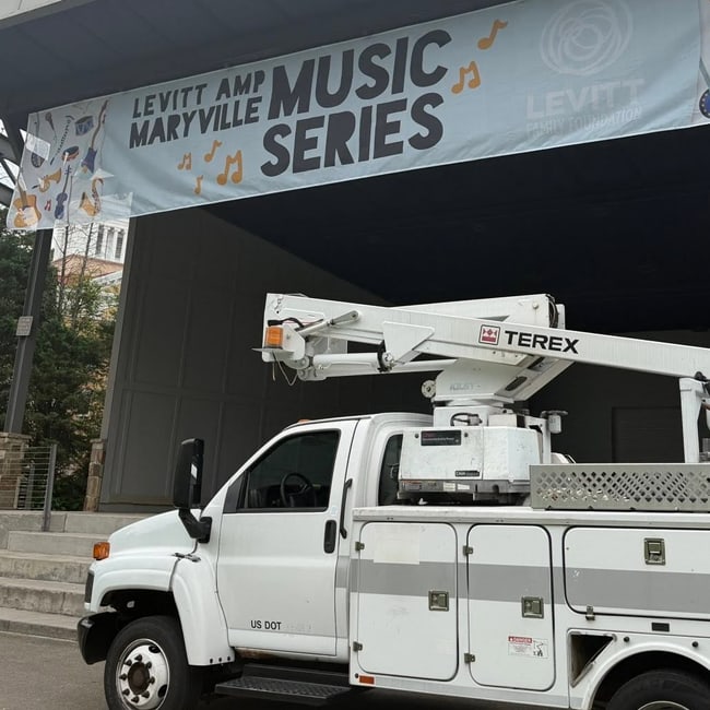 Bucket truck sitting outside of an outdoor stage with a large banner hanging from the ceiling of the stage