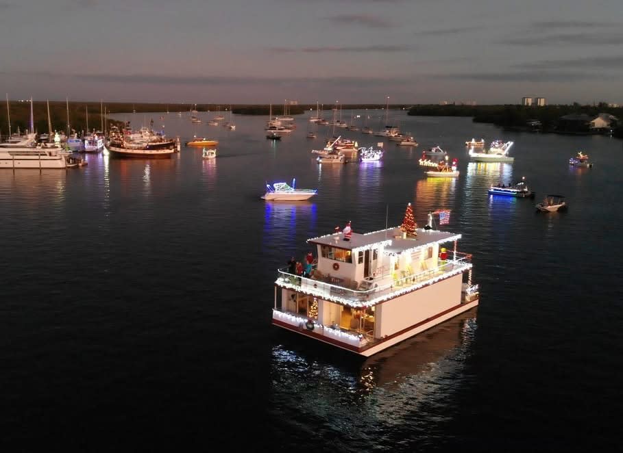 Aerial dusk view: lit houseboat with Christmas tree among anchored boats