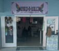 Salon entrance with a purple “Divas‑N‑Dolls” sign, open door, braided mannequin heads, and a pricing display.