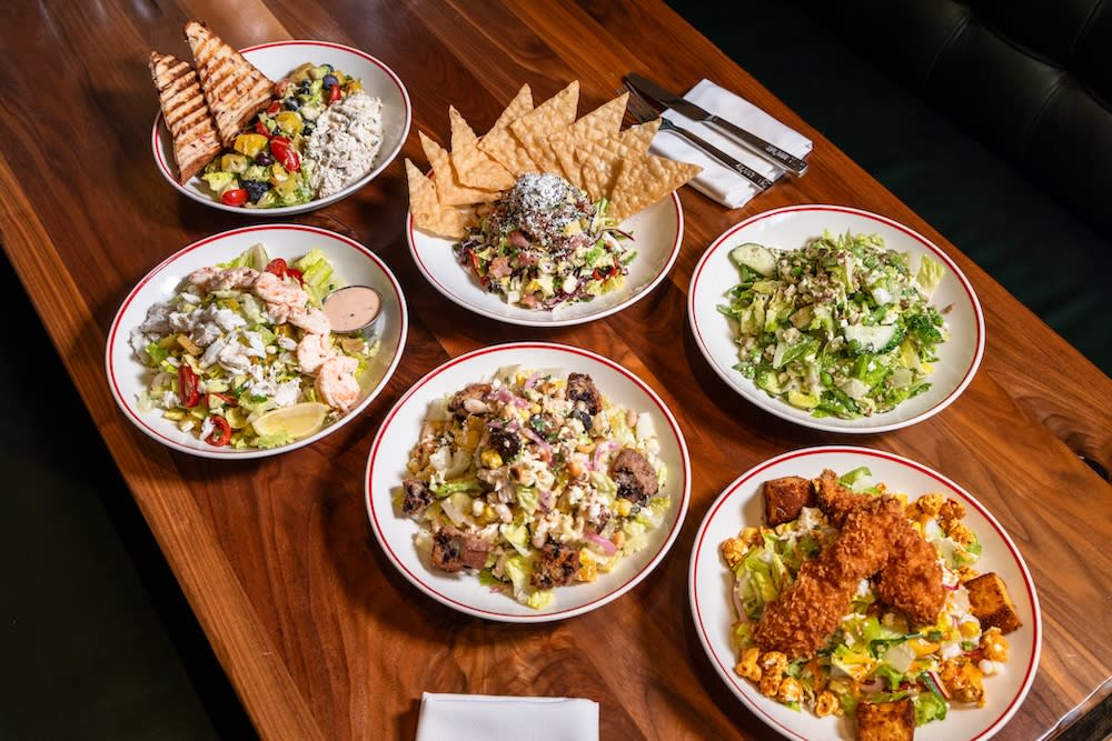 Six salads on a walnut table including crab and shrimp Louie, fried chicken, chicken salad with grilled flatbread