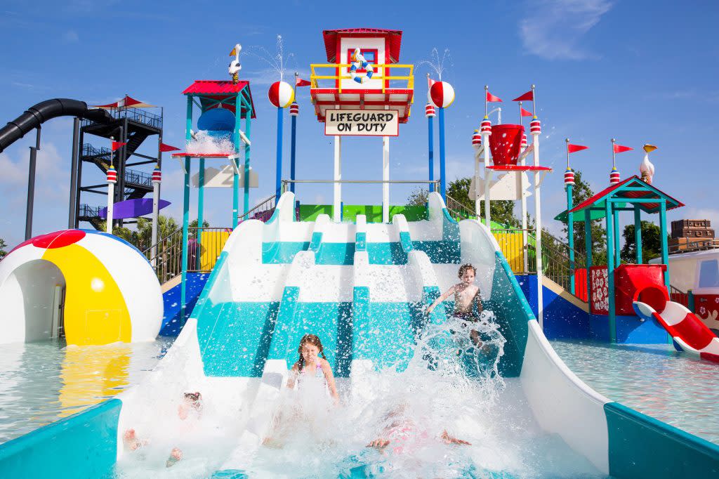 Children sliding down a small teal and white striped water slide at Summer Waves