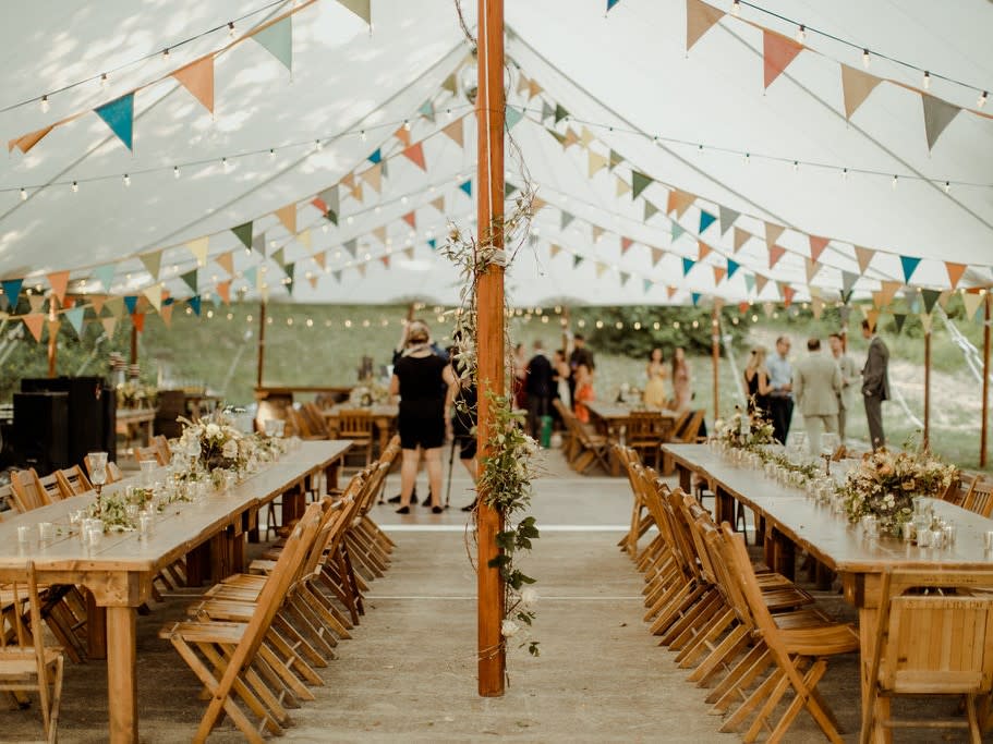 Farm tables and chair under a sailcloth tent for event