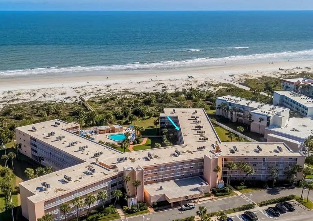 Aerial view of the St. Augustine Beach and Tennis Club complex, beach, and ocean, with a blue arrow marking the building.