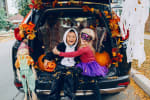 A photo of two kids in costumes sitting in an open trunk decorated for Halloween.