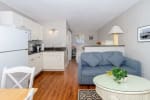 Open-concept kitchen and living area with white cabinets, hardwood floors, blue sofa, and glass coffee table.