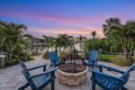 Stone fire pit surrounded by four blue Adirondack chairs on waterfront patio at twilight.