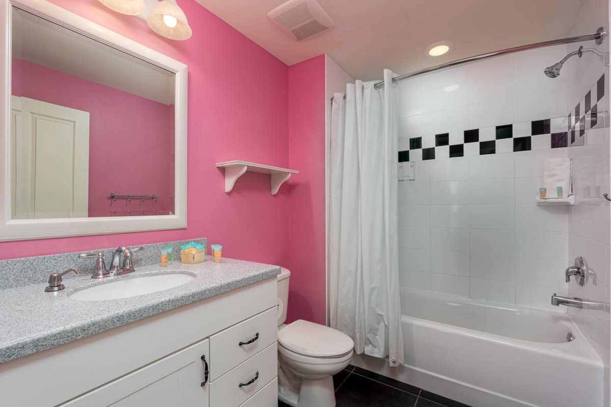 Bright bathroom with pink walls, white vanity, granite countertop, and checkered shower accents