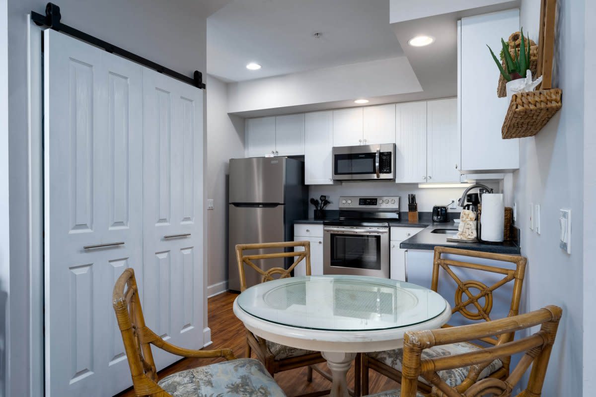Compact kitchen with white cabinets, stainless appliances, glass table, and barn door