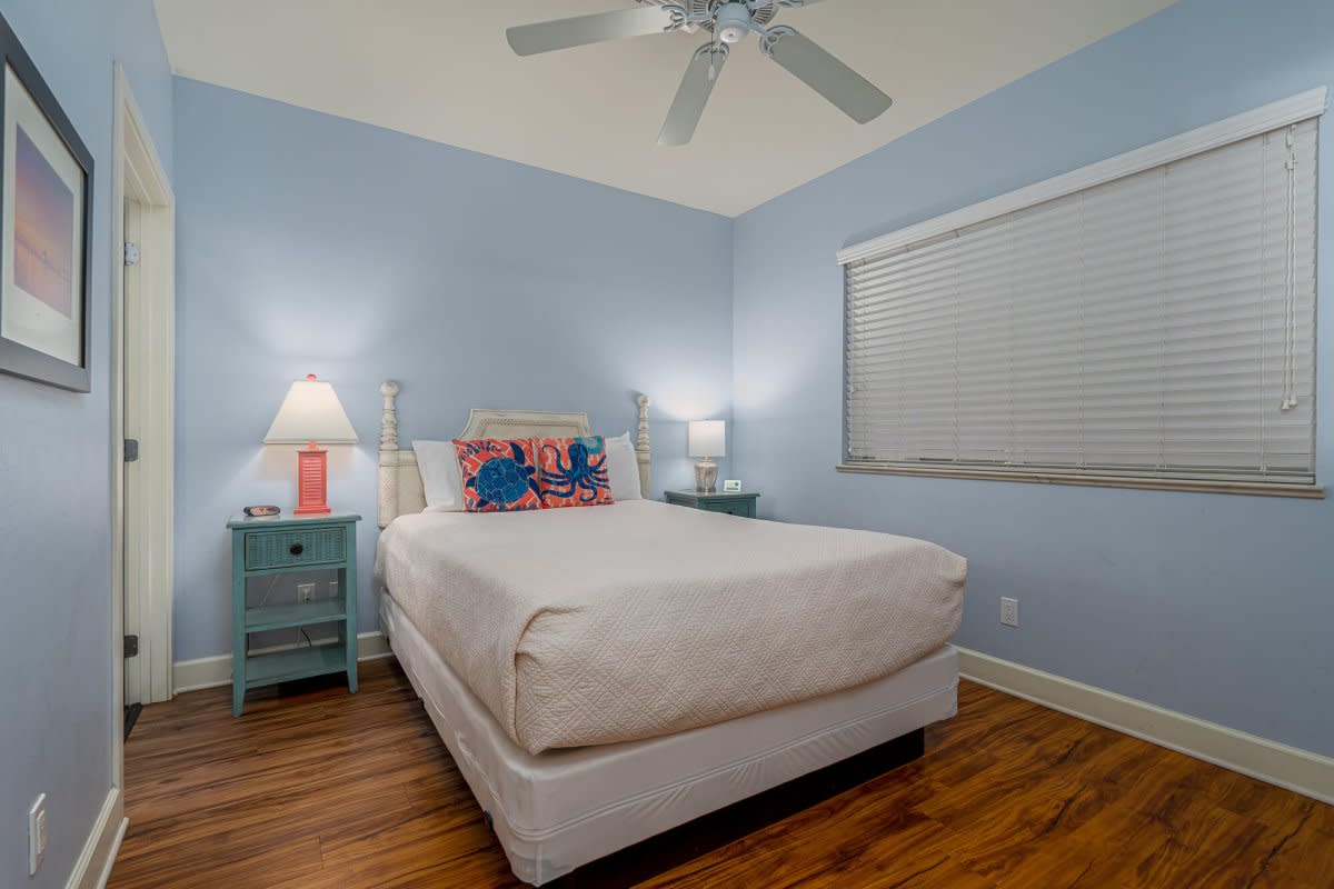 Light blue bedroom with queen bed, teal nightstands, octopus pillow, and hardwood floors