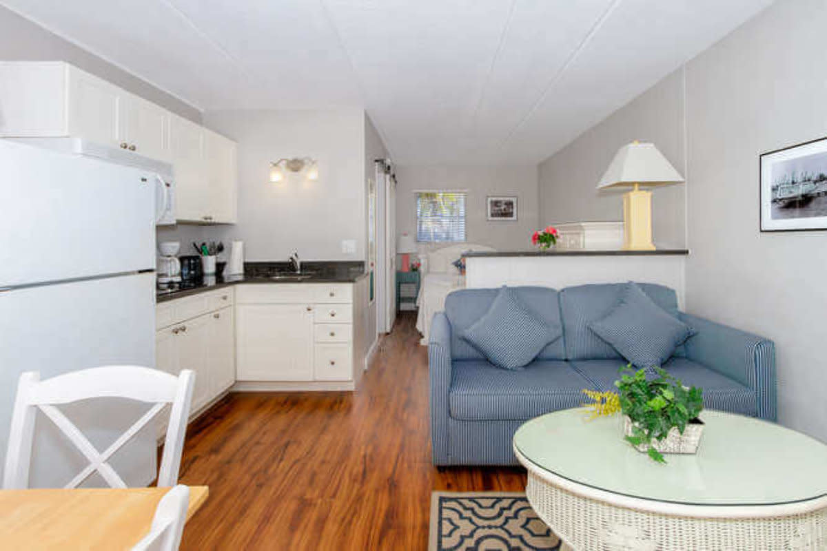 Open-concept kitchen and living area with white cabinets, hardwood floors, blue sofa, and glass coffee table.