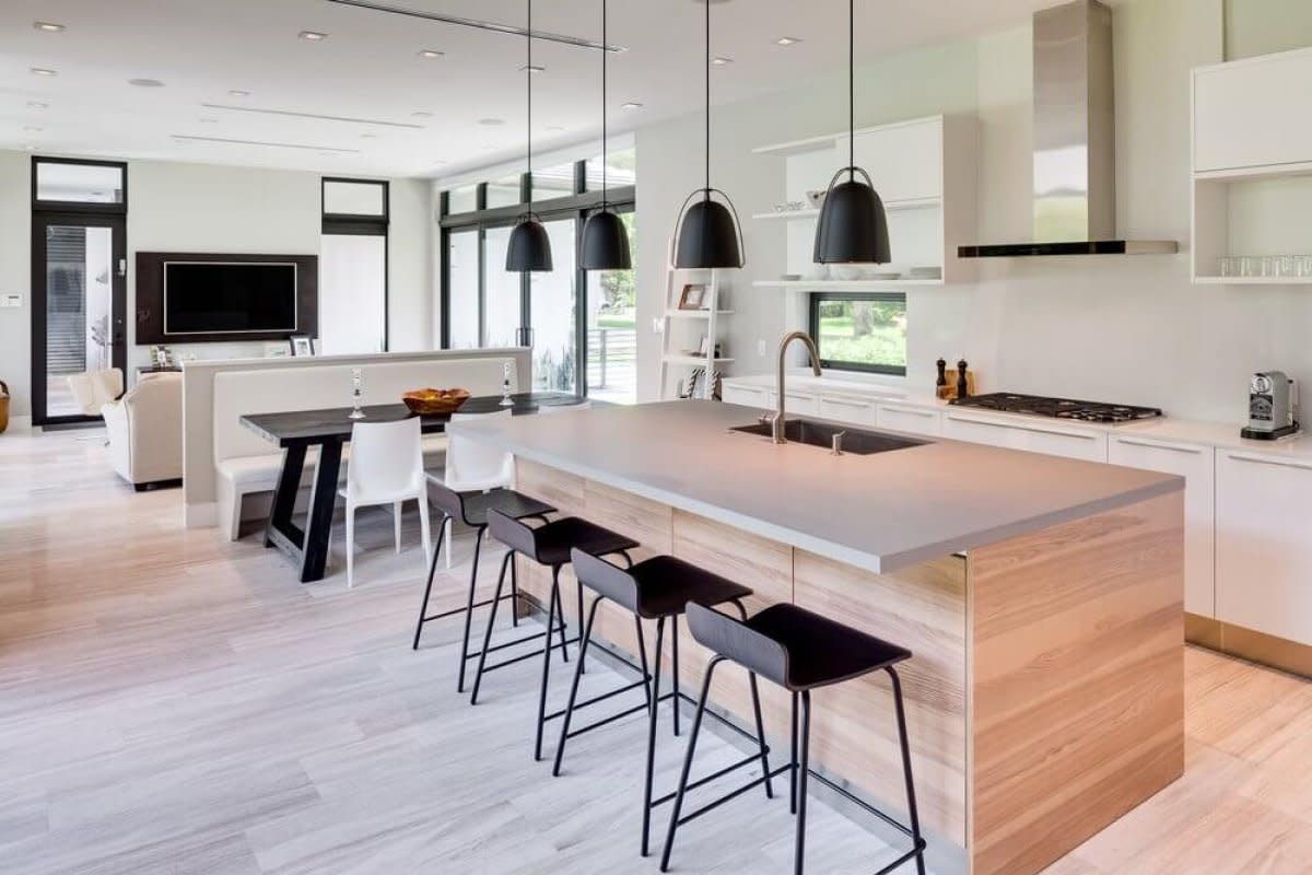 Modern kitchen with wooden island, black bar stools, pendant lighting, and open dining area.