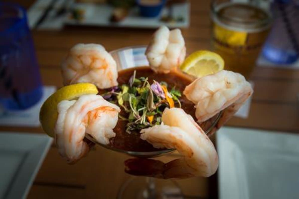 Shrimp cocktail in martini glass with cocktail sauce, lemon wedges, and microgreens garnish.