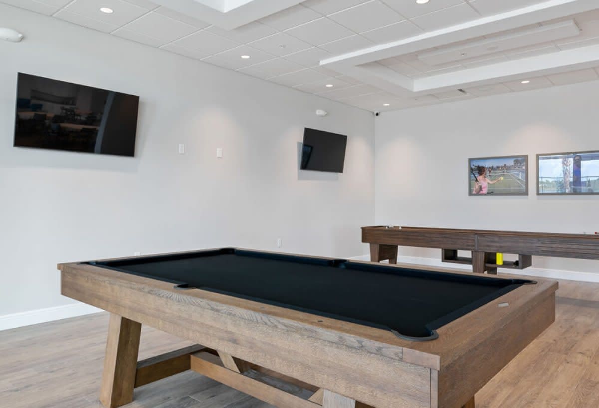 Indoor game room with wood pool table, shuffleboard and wall-mounted TVs
