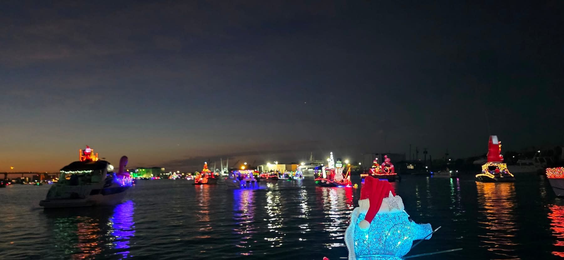 Wide view of many light-covered boats on dark water, colorful reflections