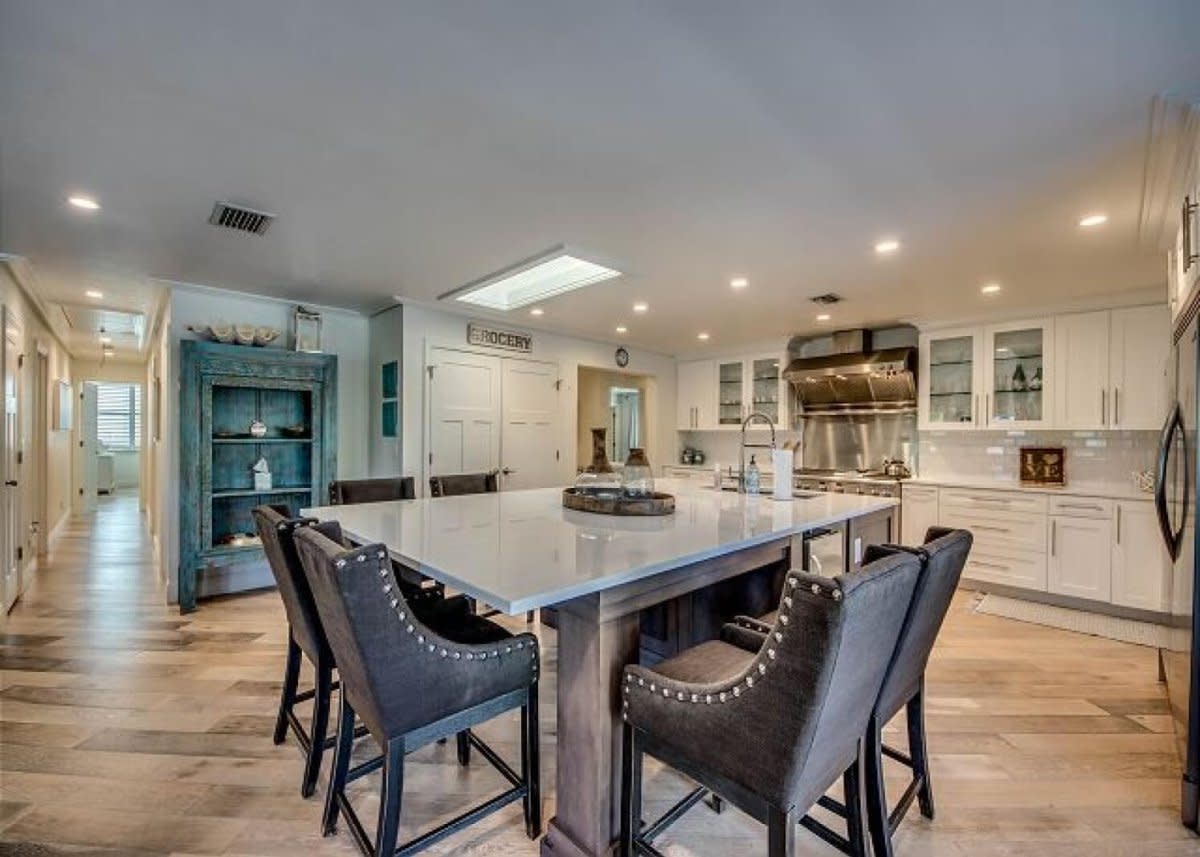 Spacious kitchen with large marble island, six bar stools, white cabinets, stainless appliances, skylight.