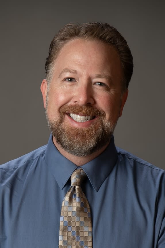 Portrait of Michael Voss, a male with brown hair and a beard, wearing a blue dress shirt with a patterned tie.