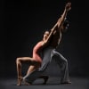 A man and woman stand back to back with their legs bent and their arms raised up