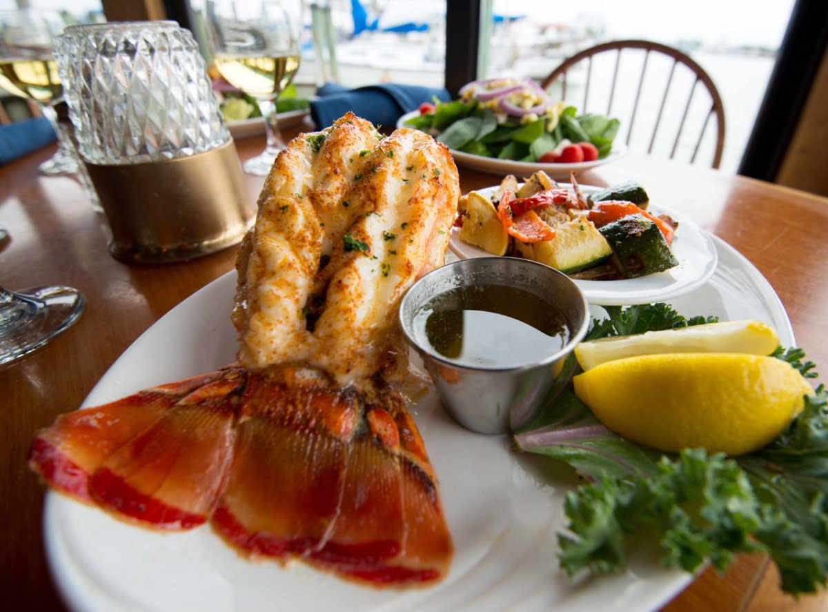 Grilled lobster tail with lemon wedges, vegetables, dipping sauce, and salad at waterfront restaurant.