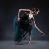 A ballet dancer in a long sheer teal skirt kneeling en pointe