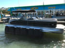 Black pontoon boat docked at Moss Marine facility with blue building and boat lounge signage visible.