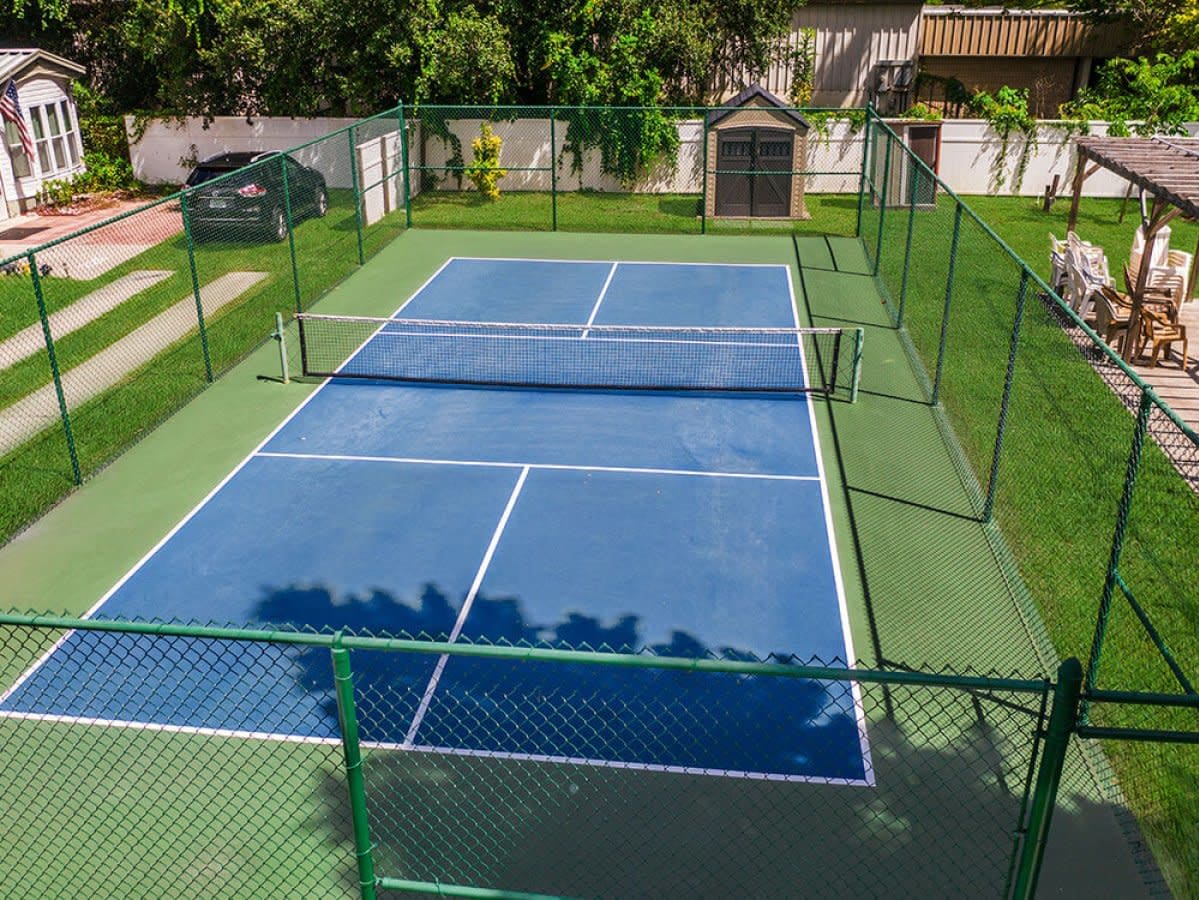 Blue tennis court with green chain-link fence and grass surrounding