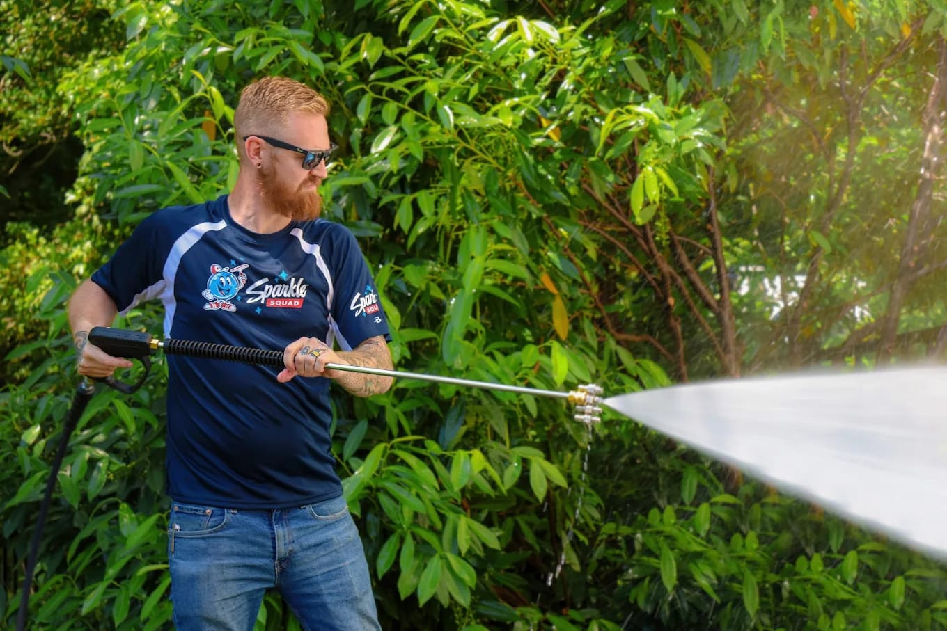 Sparkle Squad technician pressure washing exterior surfaces with high-powered equipment.