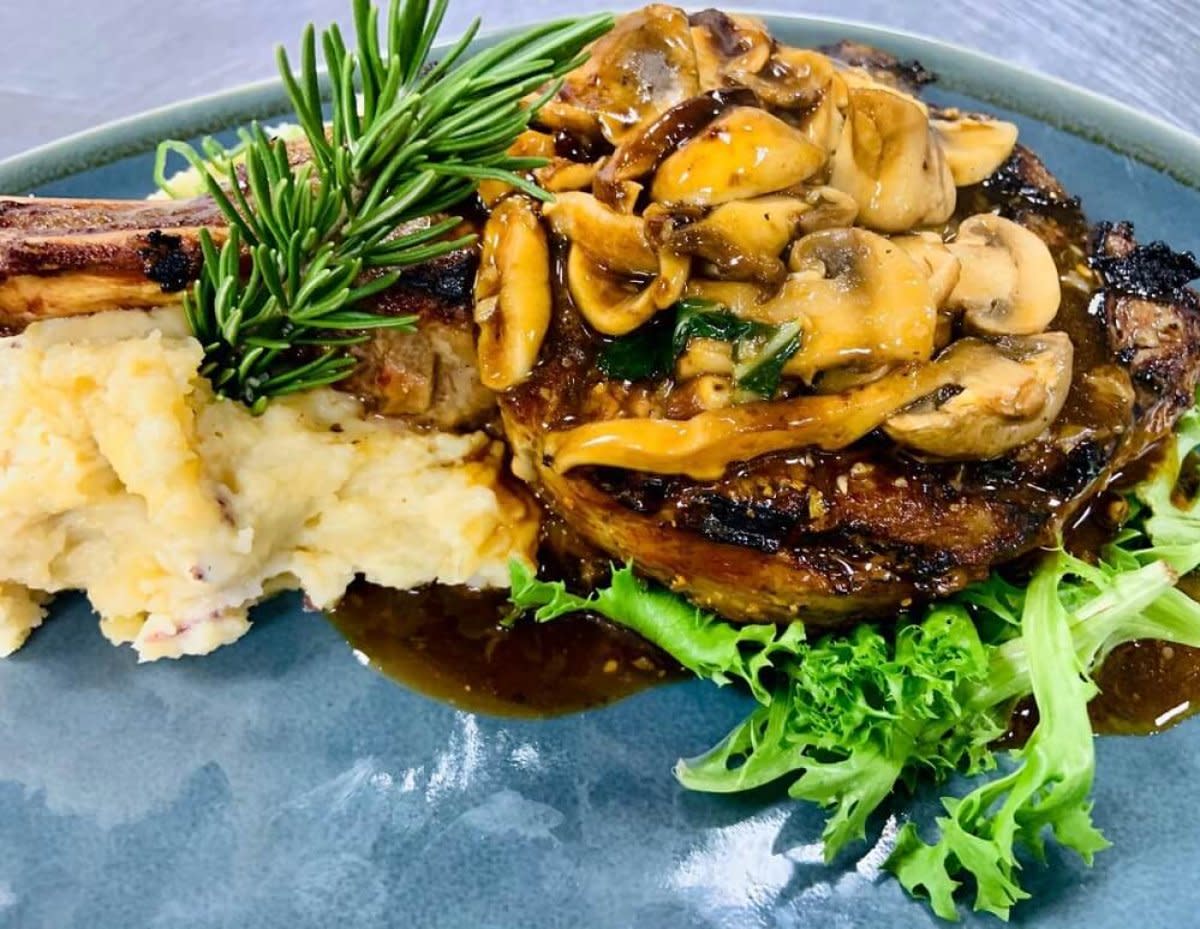 Steak topped with mushrooms served over mashed potatoes with rosemary sprig
