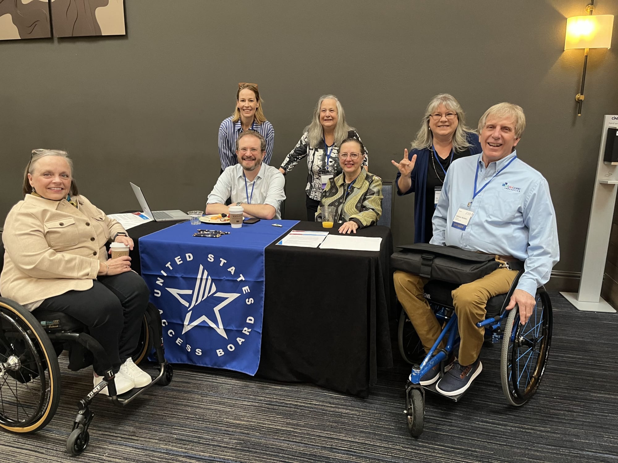 A group of individuals gathered around the Access Board's exhibitor table at the conference.