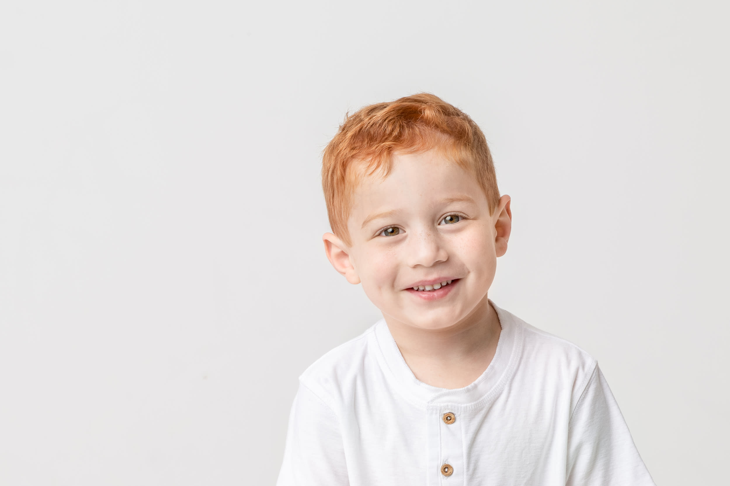 Portrait of young boy with red hair softly smiling in white shirt with white background
