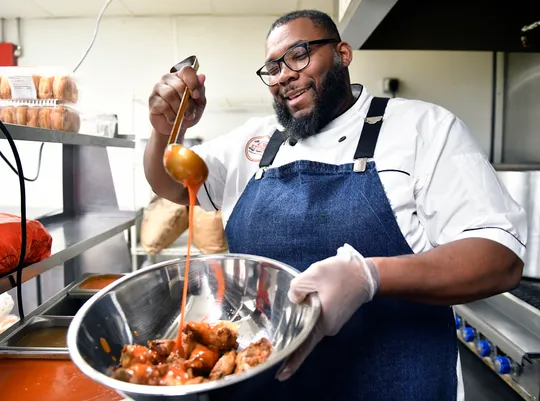 The Wing Kitchen owner Timothy Witcher drizzles his special Buffalo sauce over a order of chicken wings on Monday.