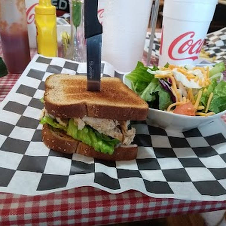 A sandwich with a knife stuck in the middle of a salad  Description automatically generated with low confidence