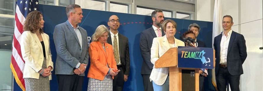 BBJ: a group of people standing around a woman at a podium