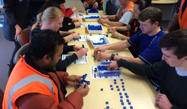 The Aeroplane Game© Simulation a table with a group of people who are building with blue Lego