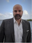 A person in a suit standing in front of water

Description automatically generated