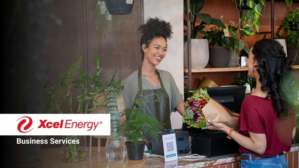 A business owner helps a customer at a cash register the Xcel Energy logo is overlayed along with the words Business Services
