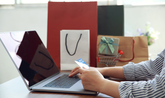 Arms of female making online gift card purchase with nearby shopping bags