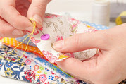 Hands sewing a button onto fabric