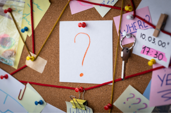 Question mark pinned on a cork board surrounded by colorful sticky notes and push pins.