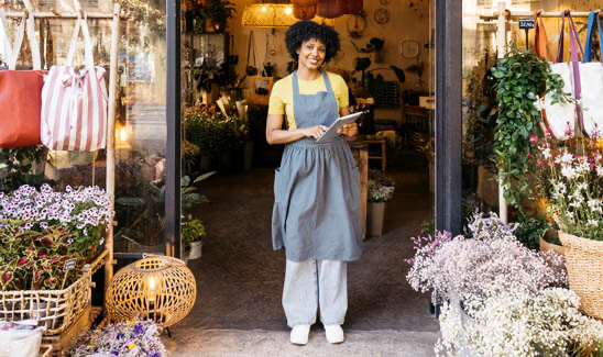 Florist owner holding digital tablet and smiling in front of her flower shop
