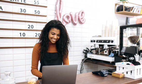 Woman employee behind coffee shop counter working on computer