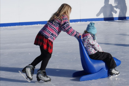 ice skating girl pushes friend in sled